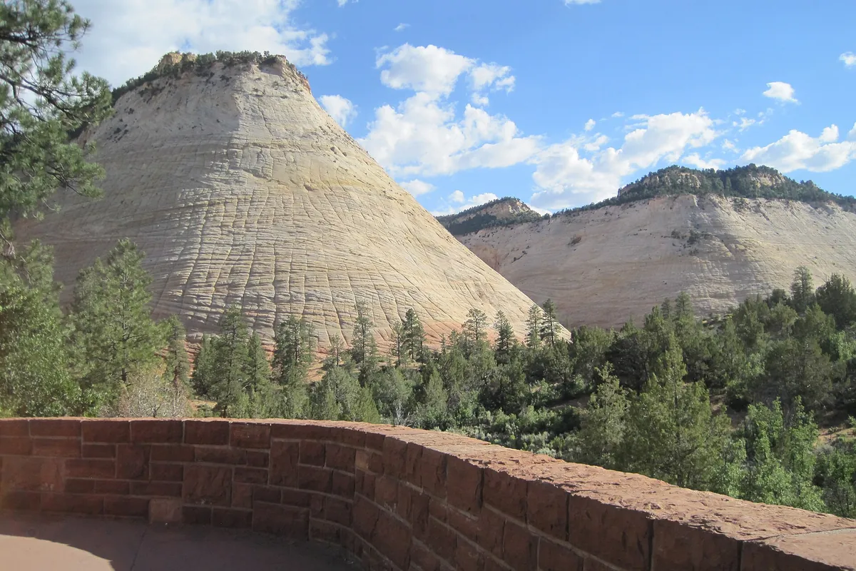 Checkerboard Mesa, a pale cross-hatched sandstone dome, seen from a stone-walled pullout on the Zion-Mount Carmel Highway