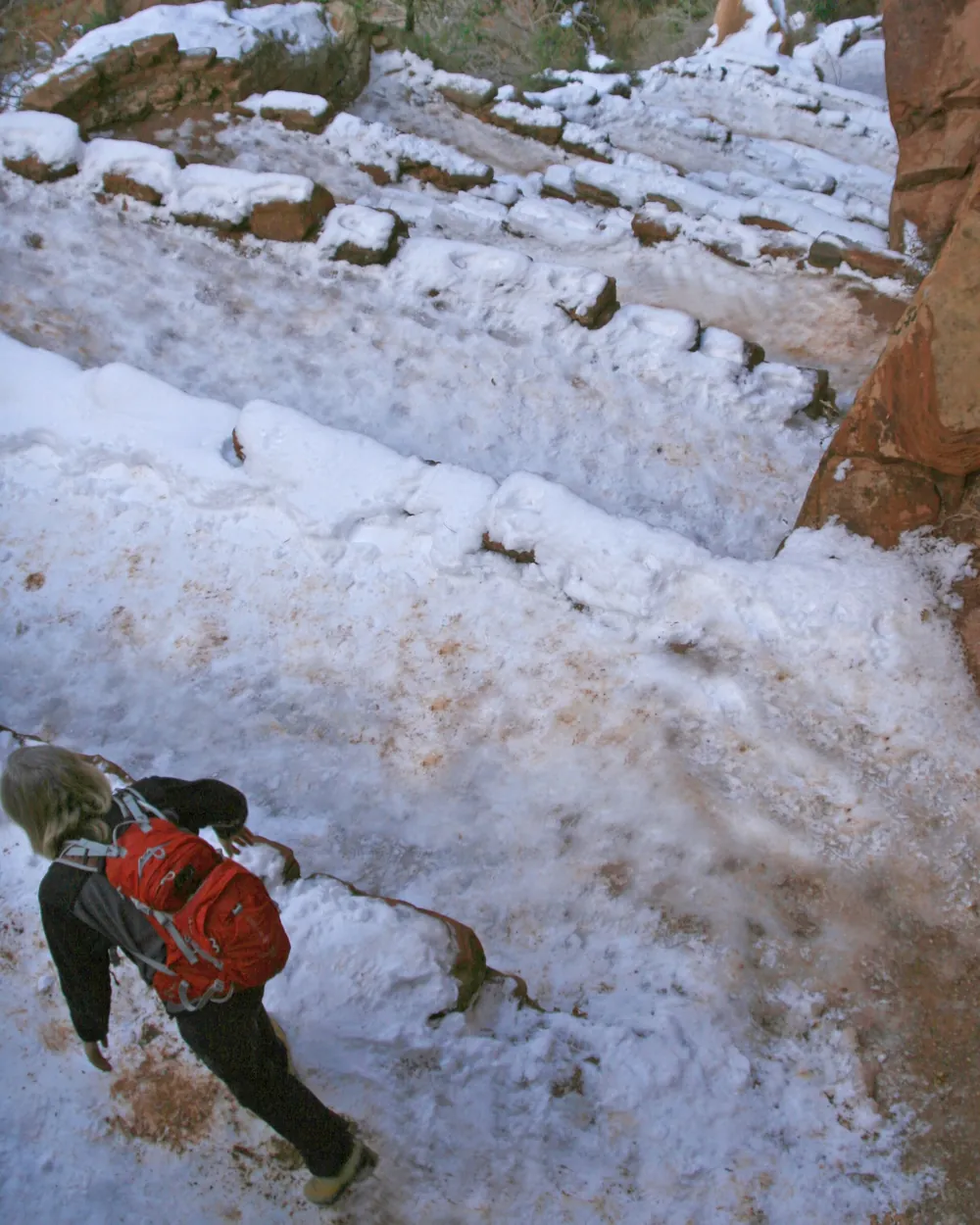A hiker in a red backpack descending snow-covered stone steps on Walter's Wiggles in winter